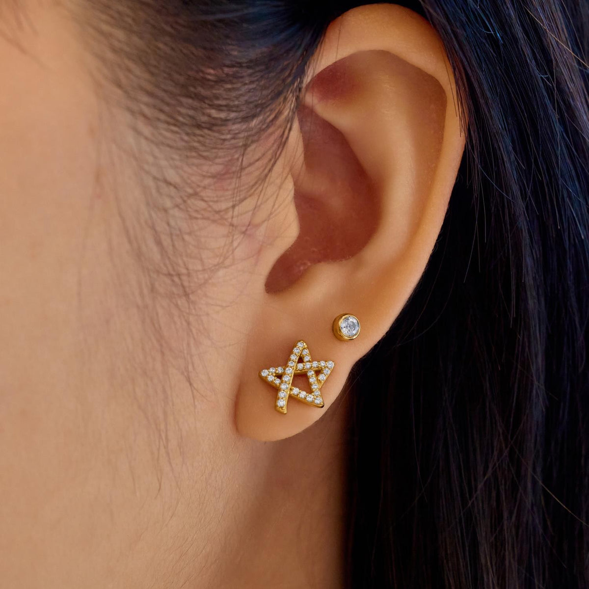Close-up of an ear wearing a star-shaped earring with a diamond.