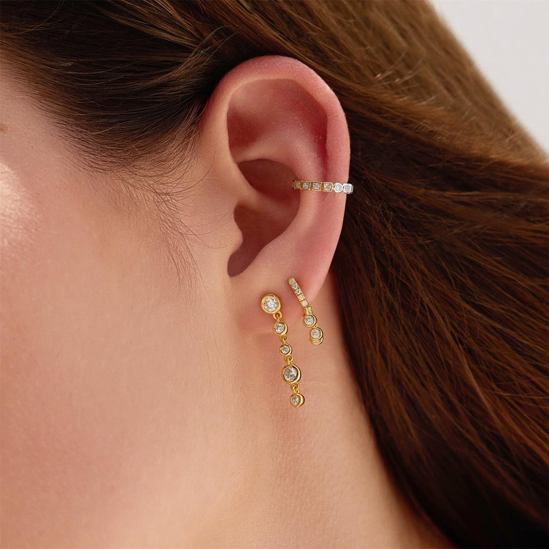 Close-up of an ear wearing gold earrings with a neutral background