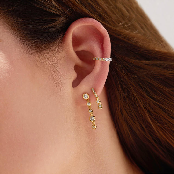 Close-up of an ear wearing gold earrings with a neutral background