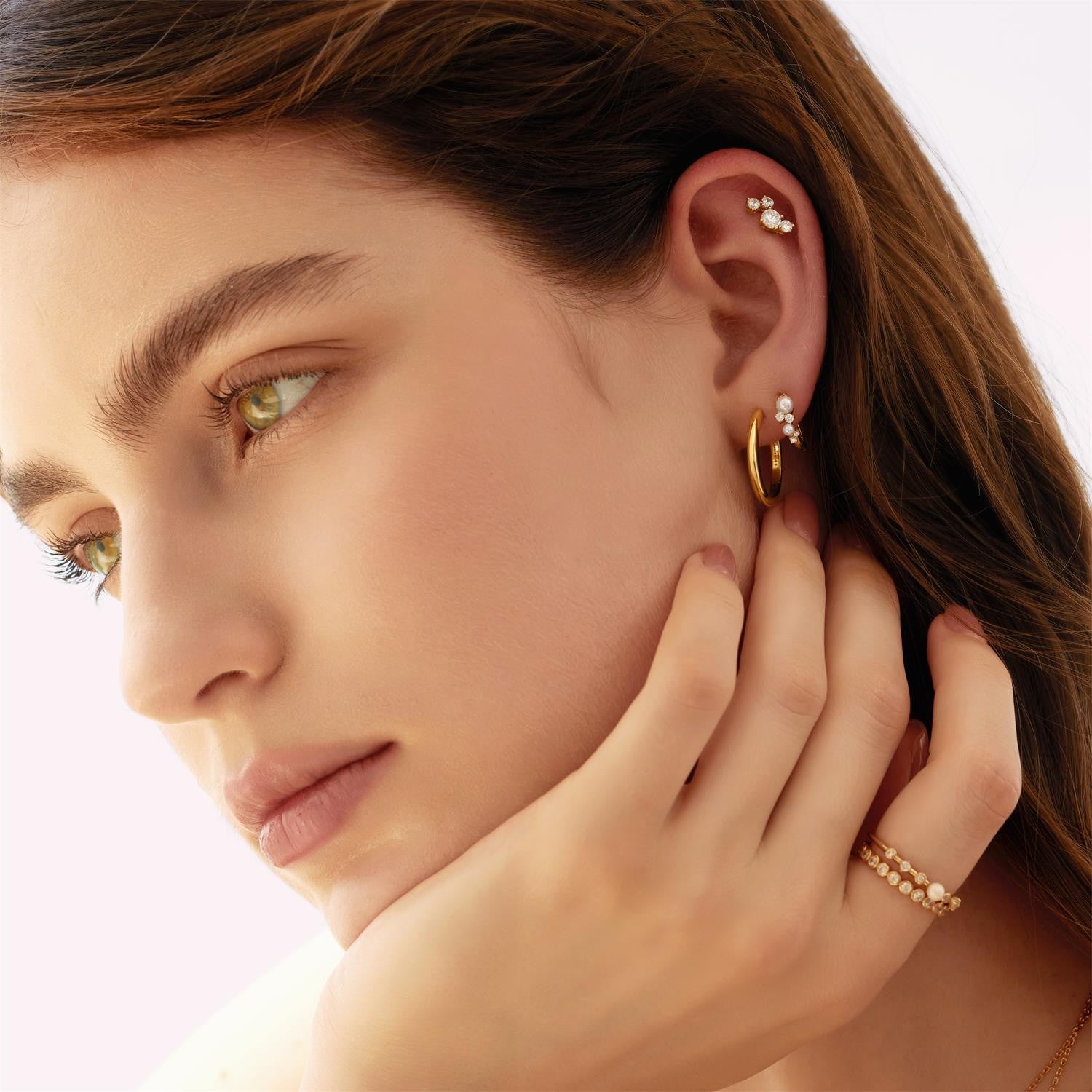 Close-up of a woman wearing gold hoop earrings and a ring, with a neutral background