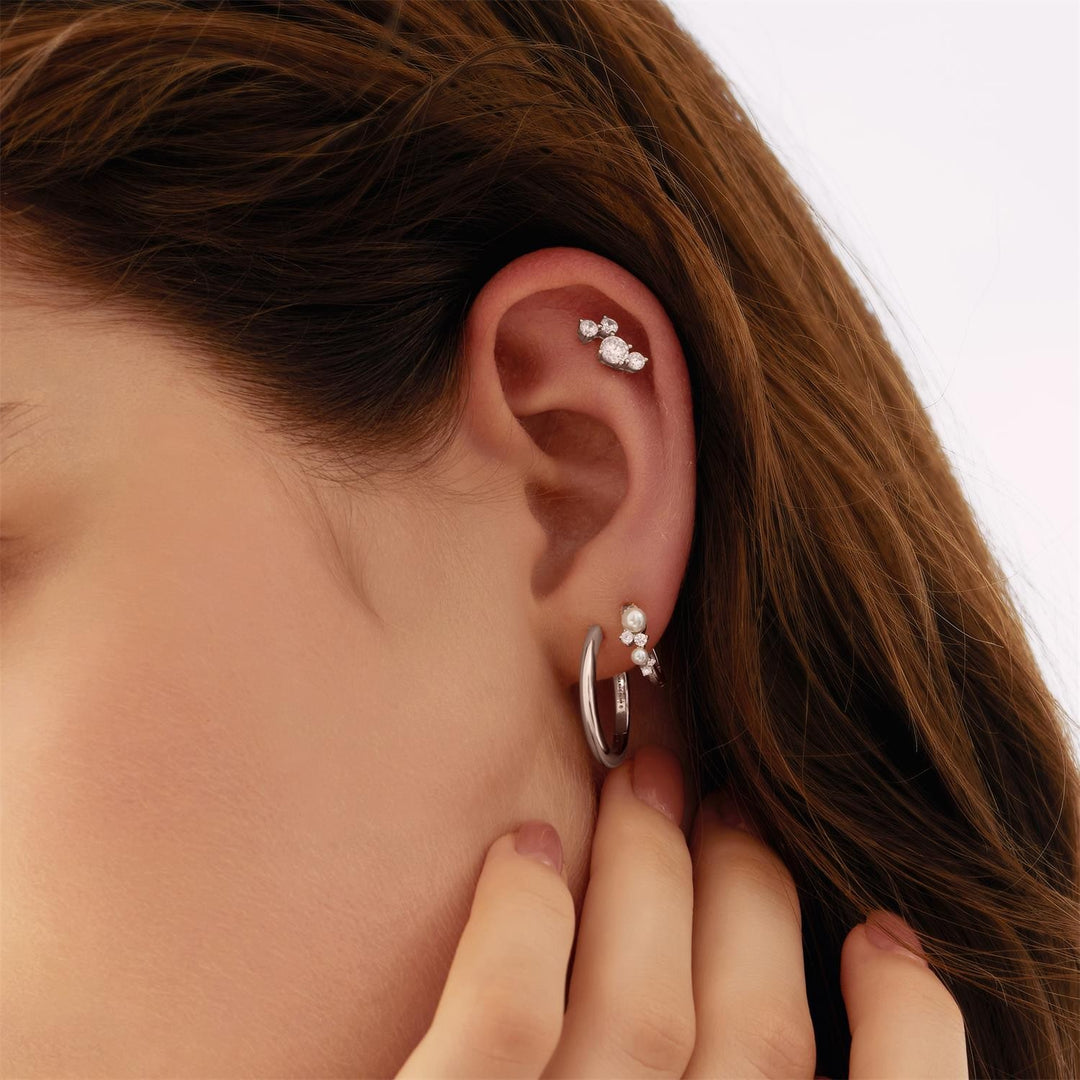 Close-up of an ear with pearl earrings and a hand adjusting them against a neutral background