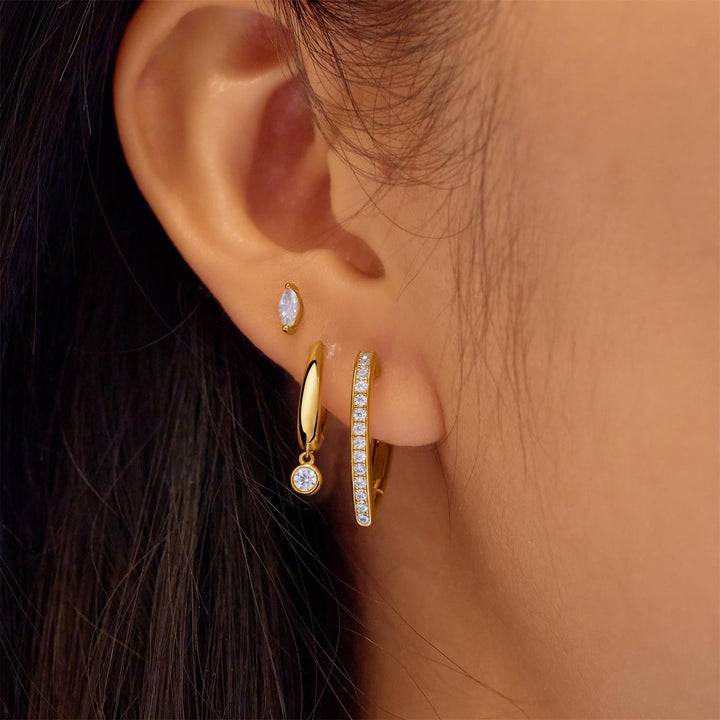 Close-up of an ear wearing gold hoop earrings with clear gemstones.