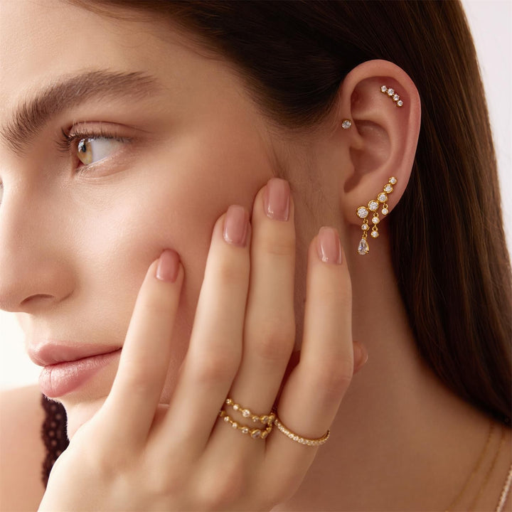 Close-up of a woman wearing gold earrings and rings with a neutral background