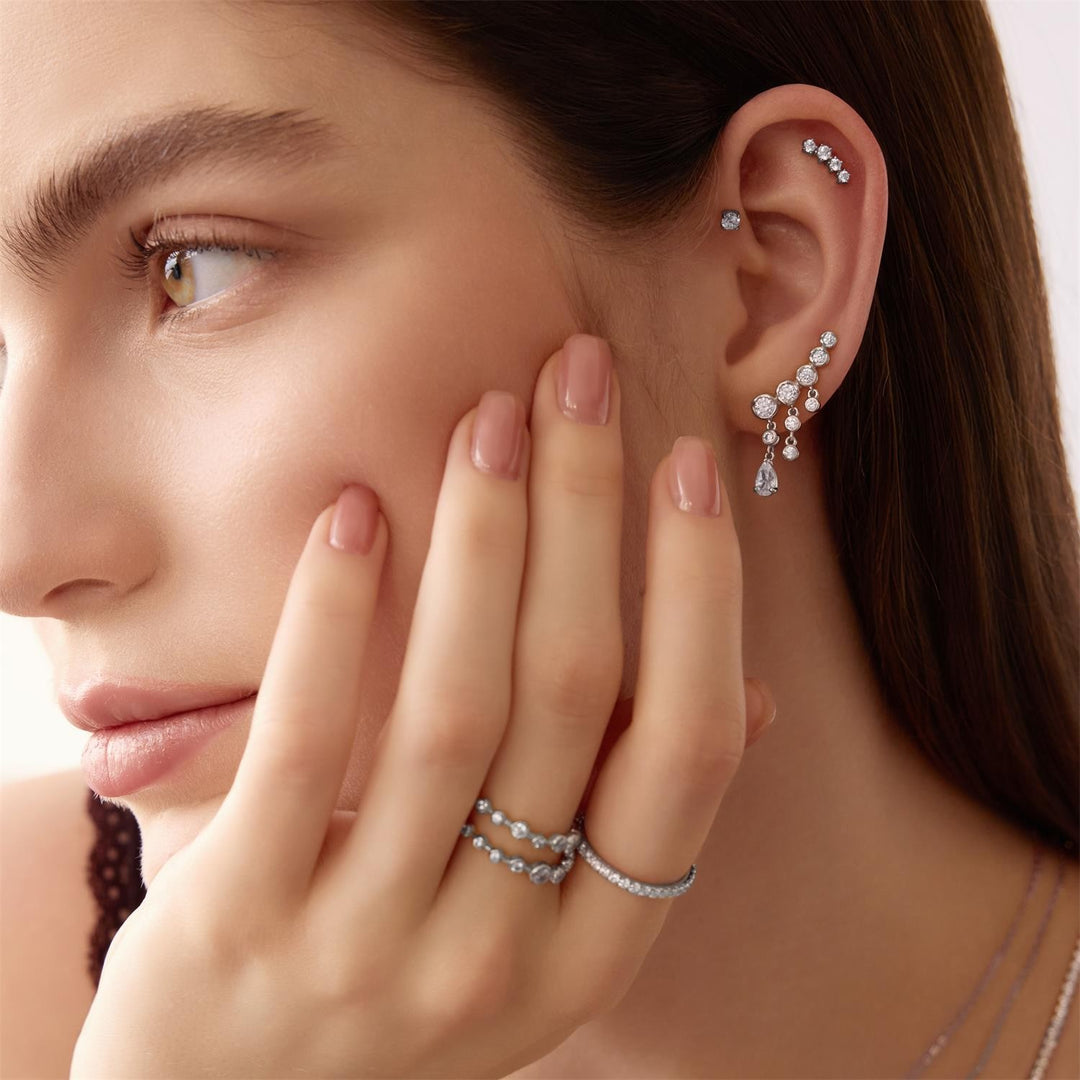 Close-up of a woman wearing silver earrings and rings, with one hand near her face.