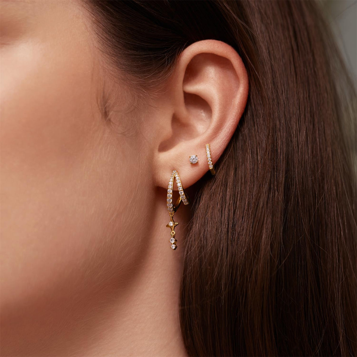 Close-up of an ear wearing gold hoop earrings with small gemstones.