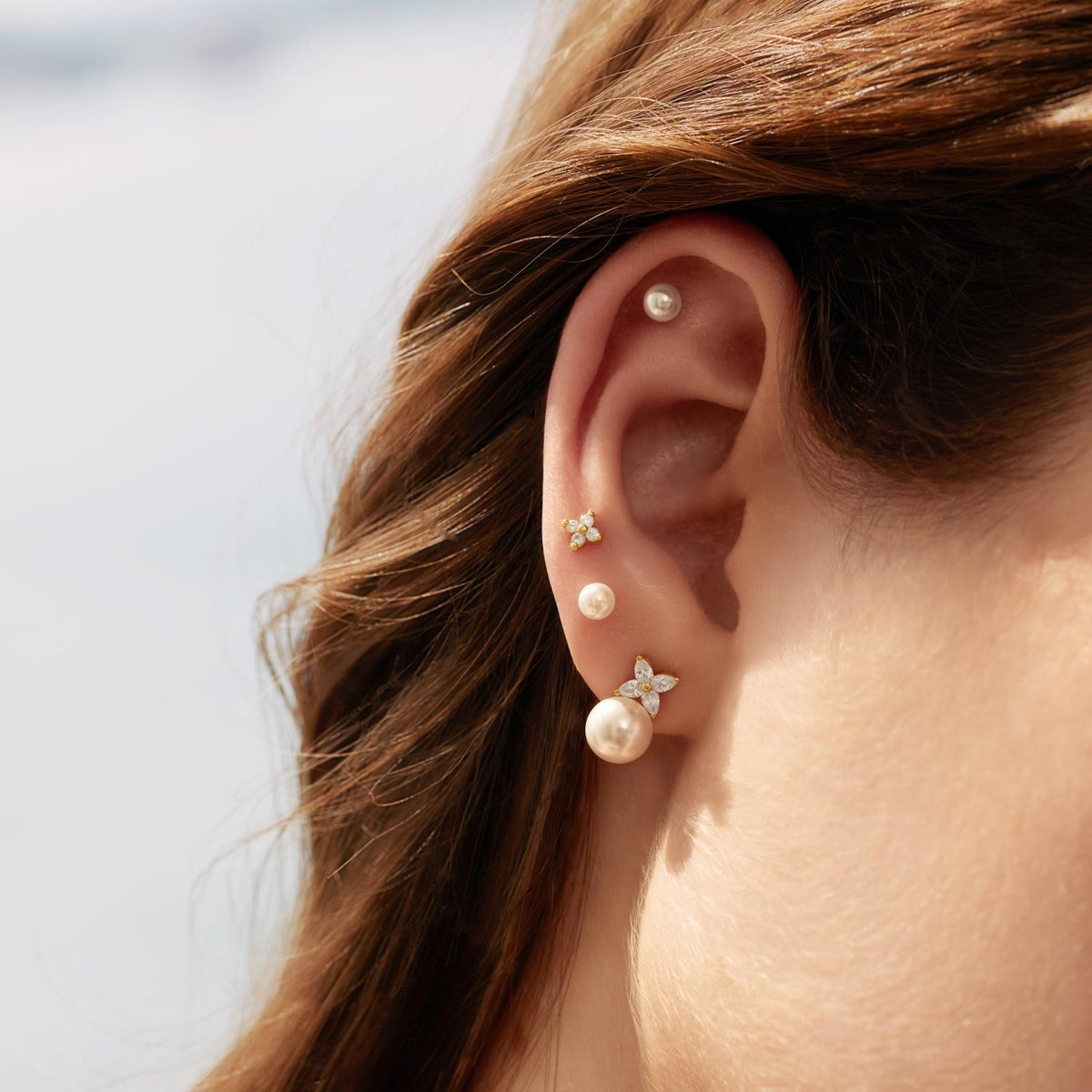 Close-up of an ear with pearl and gold earrings against a blurred background