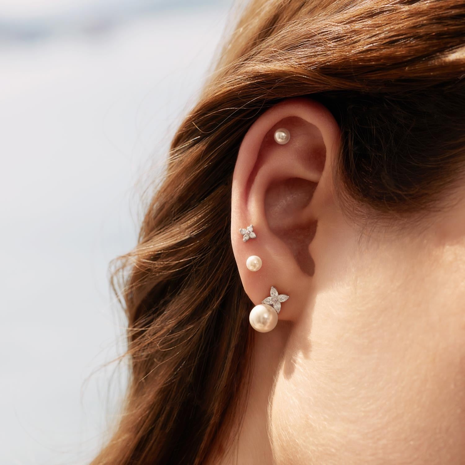 Close-up of an ear wearing pearl and star-shaped earrings with a blurred background