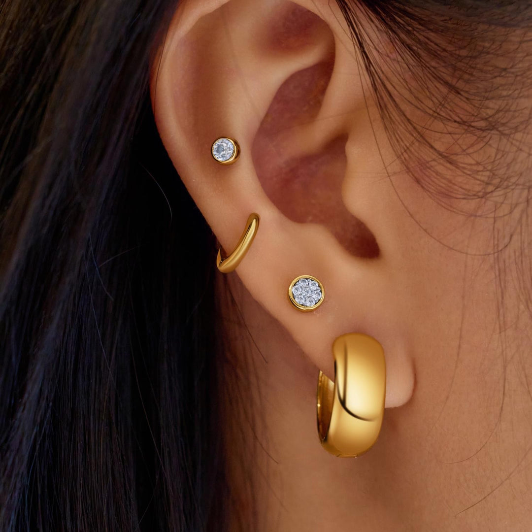 Close-up of an ear wearing gold hoop earrings and diamond stud earrings.