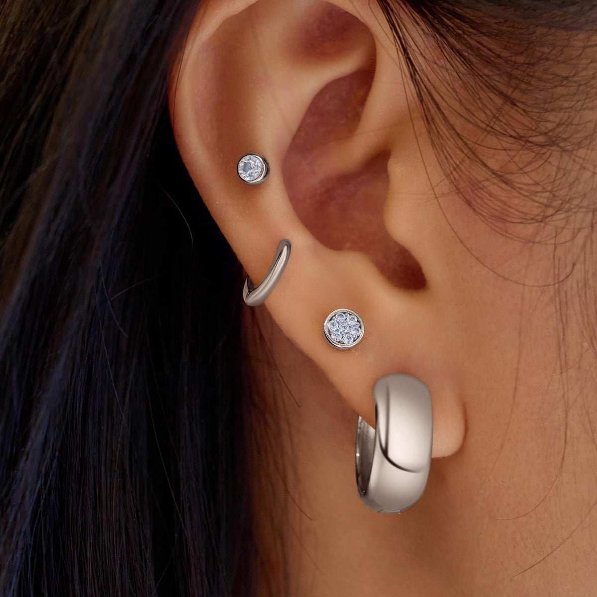 Close-up of an ear wearing silver earrings with gemstones.