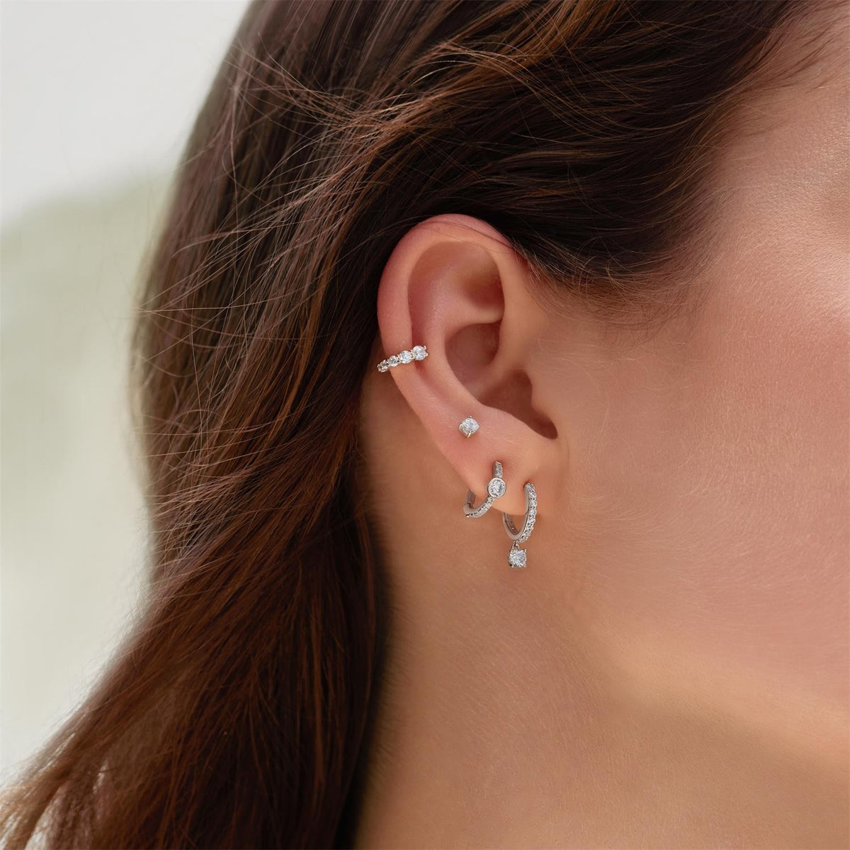 Close-up of an ear wearing multiple diamond earrings with a blurred background