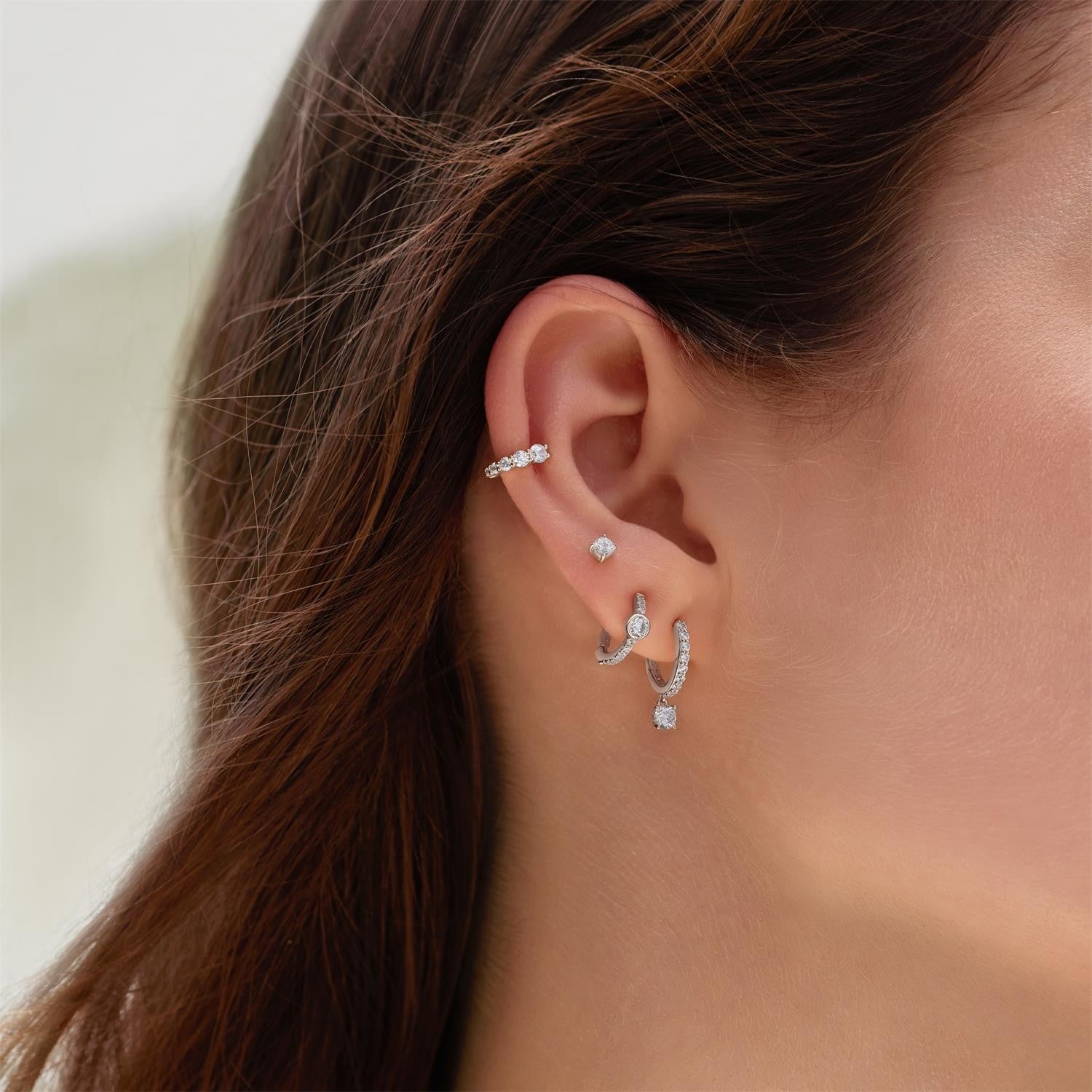 Close-up of an ear wearing multiple diamond earrings with a blurred background