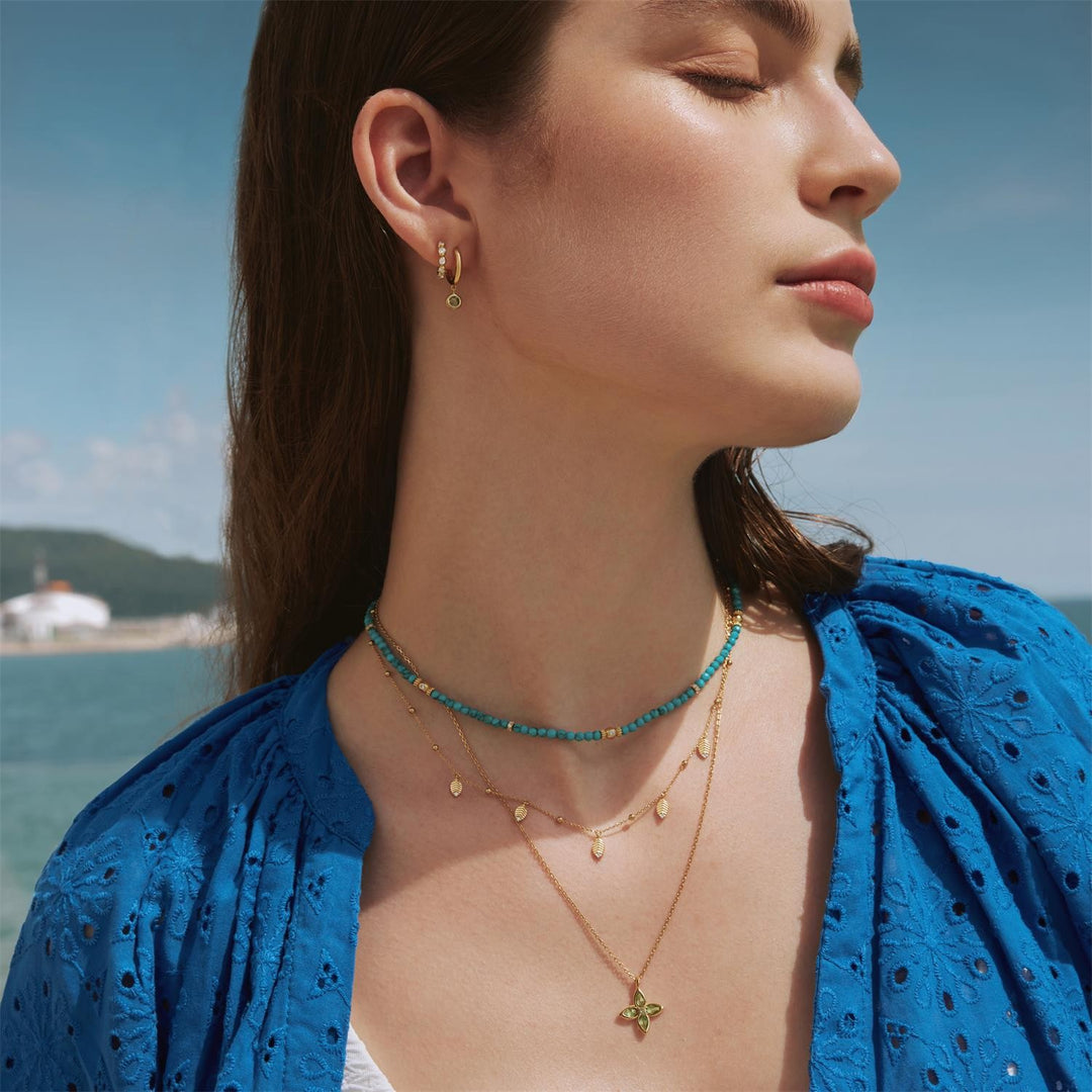 Woman wearing gold and turquoise necklaces with a blue top against a scenic background