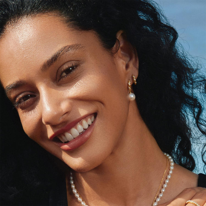 Woman wearing pearl earrings and necklace with a blurred natural background
