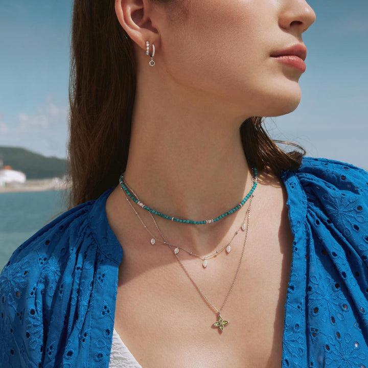 Woman wearing a blue top with layered necklaces by the water