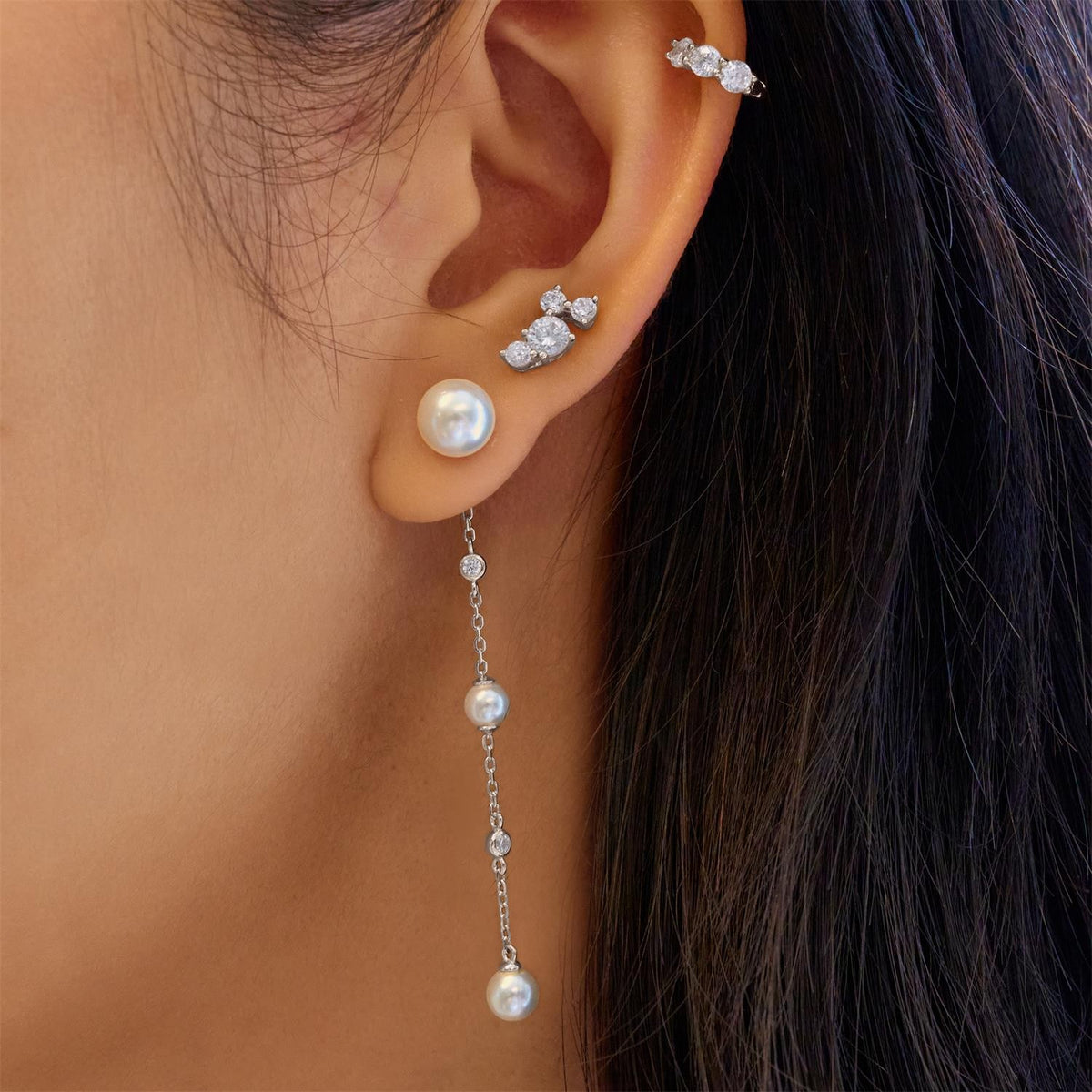 Close-up of an ear wearing pearl and crystal earrings with a blurred background