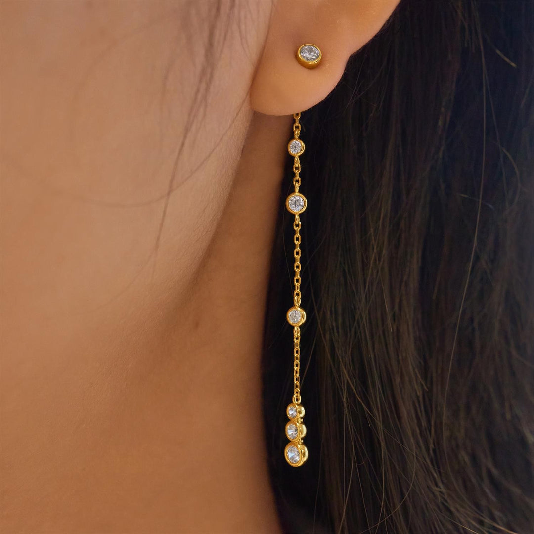 Gold chain earring with small diamonds worn by a person with dark hair.