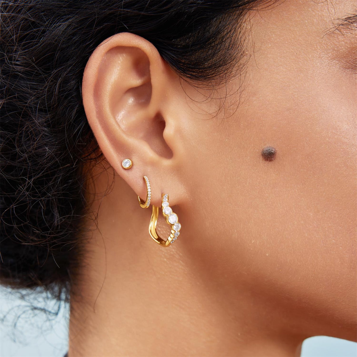 Close-up of an ear wearing gold hoop earrings with small gemstones.