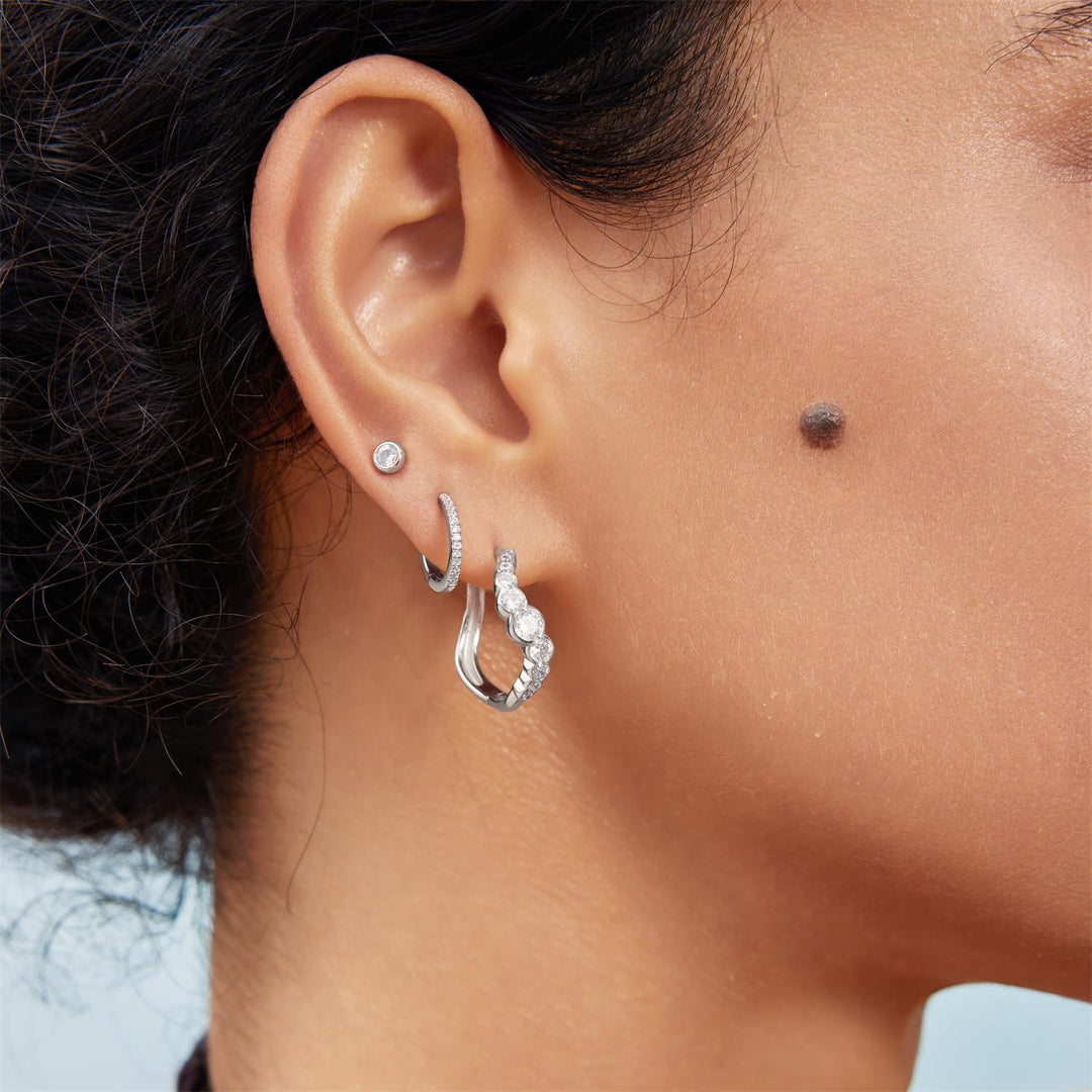 Close-up of an ear wearing silver hoop earrings with a light background