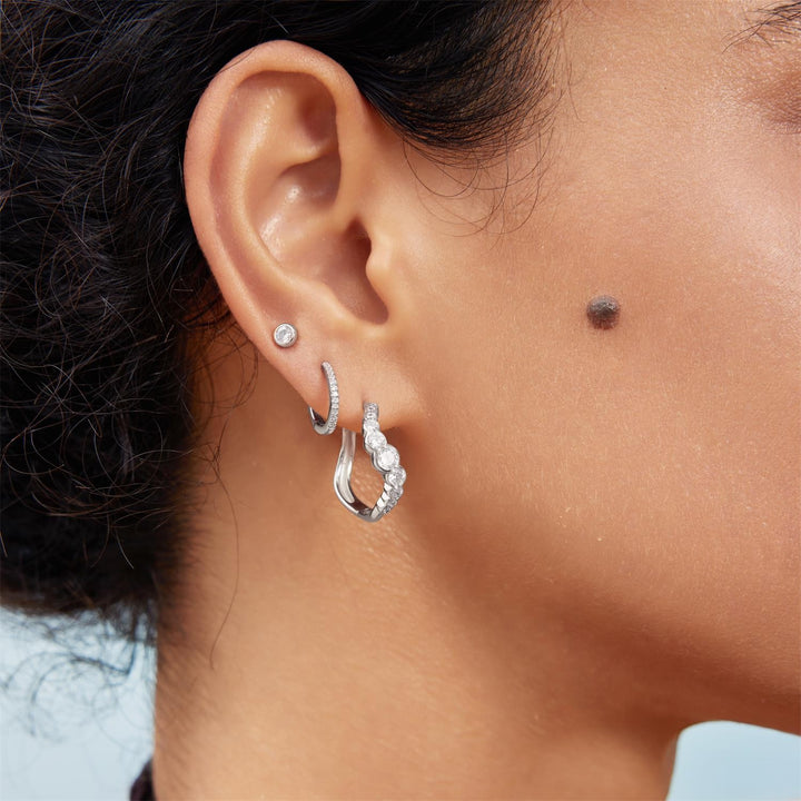 Close-up of an ear wearing silver hoop earrings with a light background
