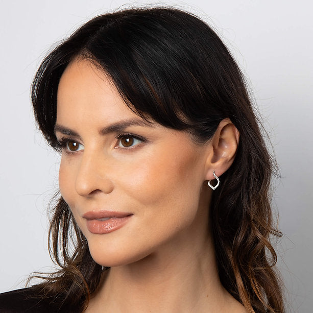 Close-up of a woman with wavy hair wearing a heart-shaped earring against a plain background