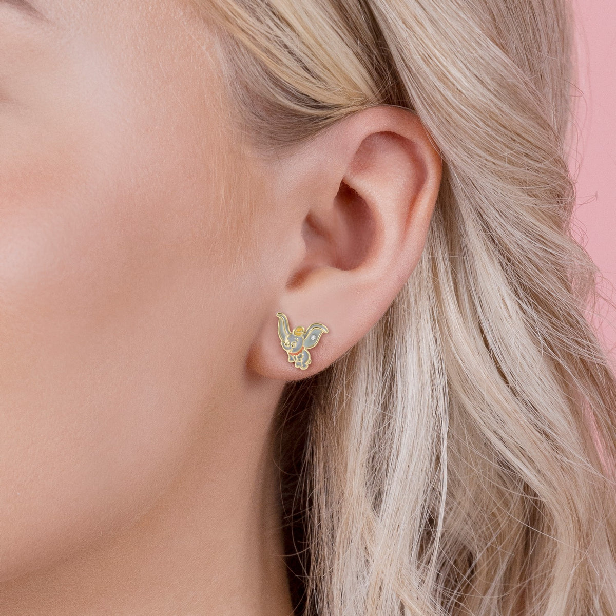 Close-up of a person wearing a butterfly-shaped earring with a pink background