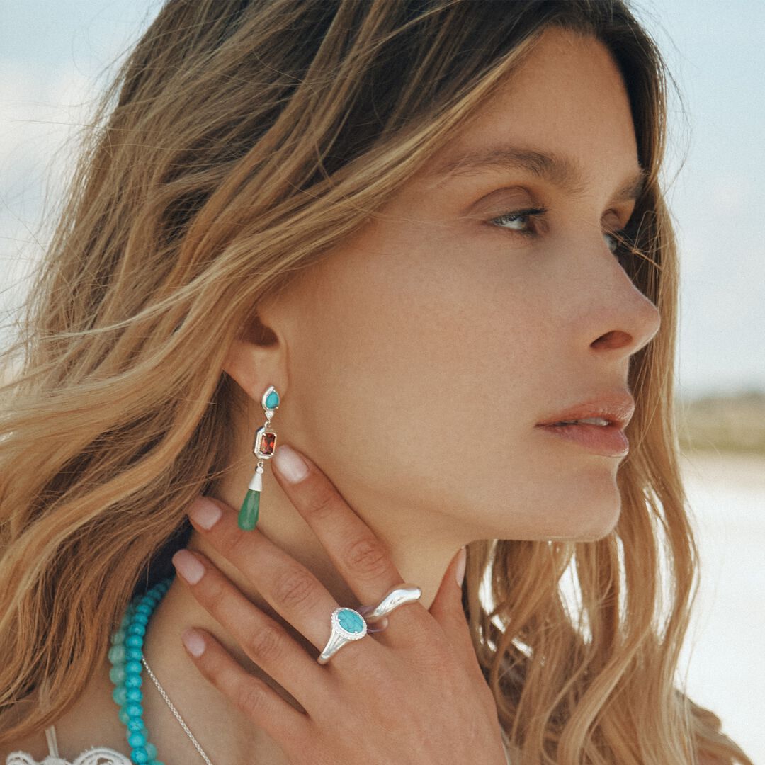 Woman wearing turquoise earrings and ring with a blurred natural background