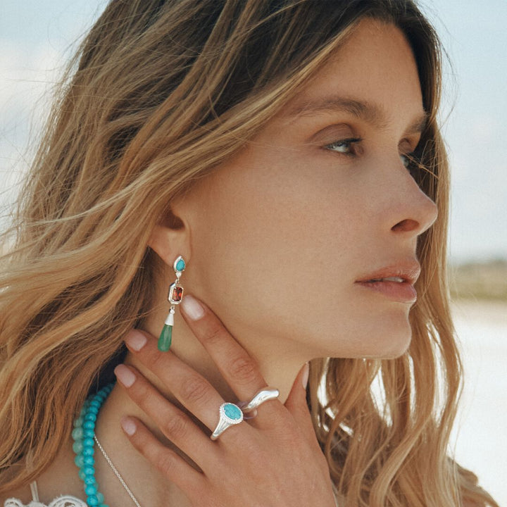 Woman wearing turquoise earrings and ring with a blurred natural background