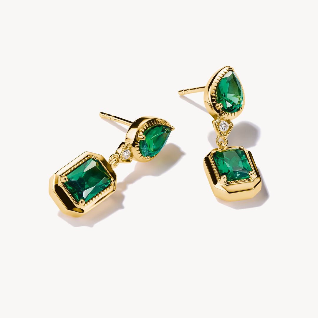 Gold earrings with green gemstones on a white background
