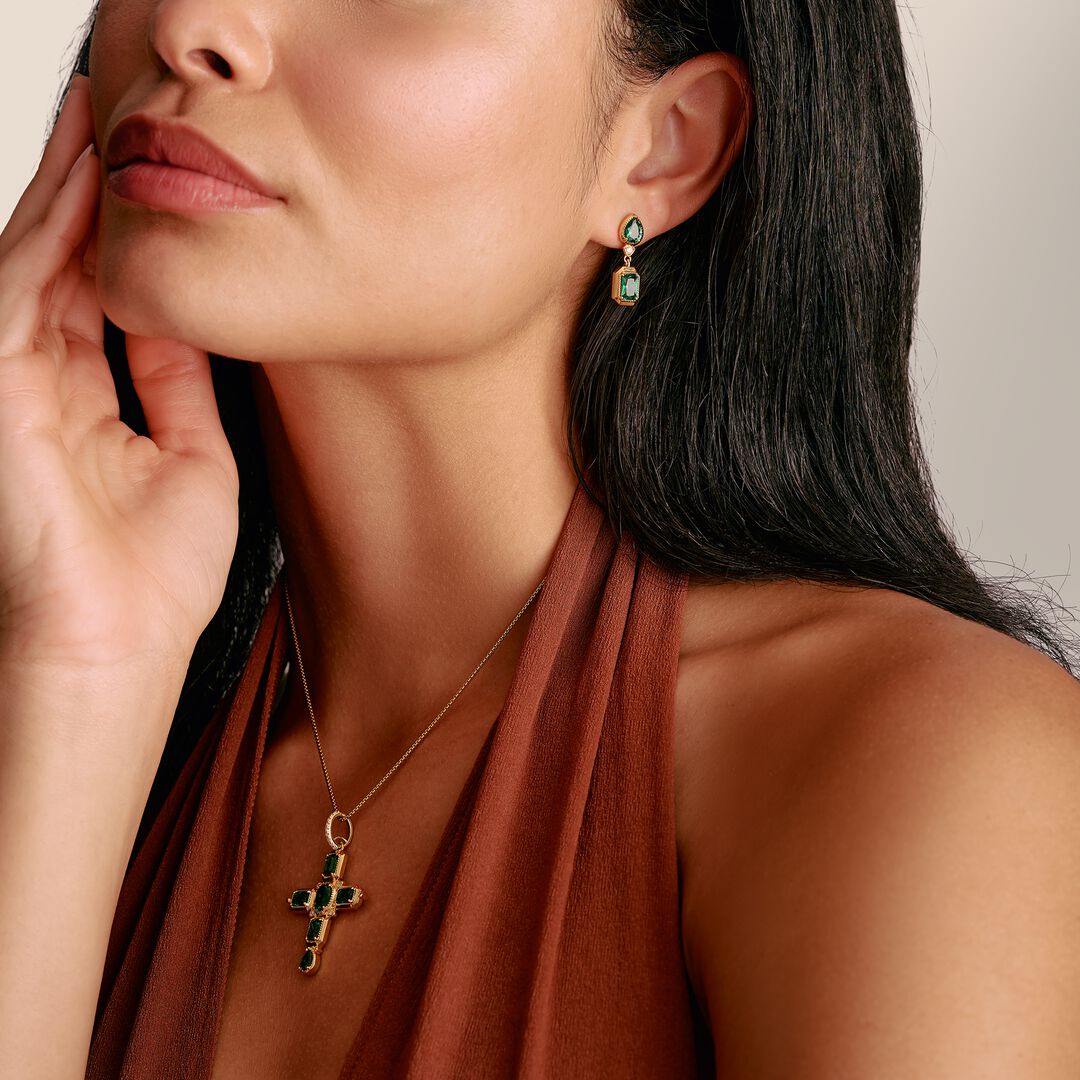 Close-up of a woman wearing gold cross necklace and earrings with green gemstones.