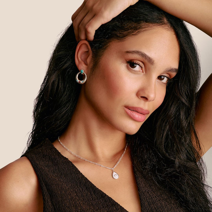 Woman wearing earrings and a necklace against a beige background