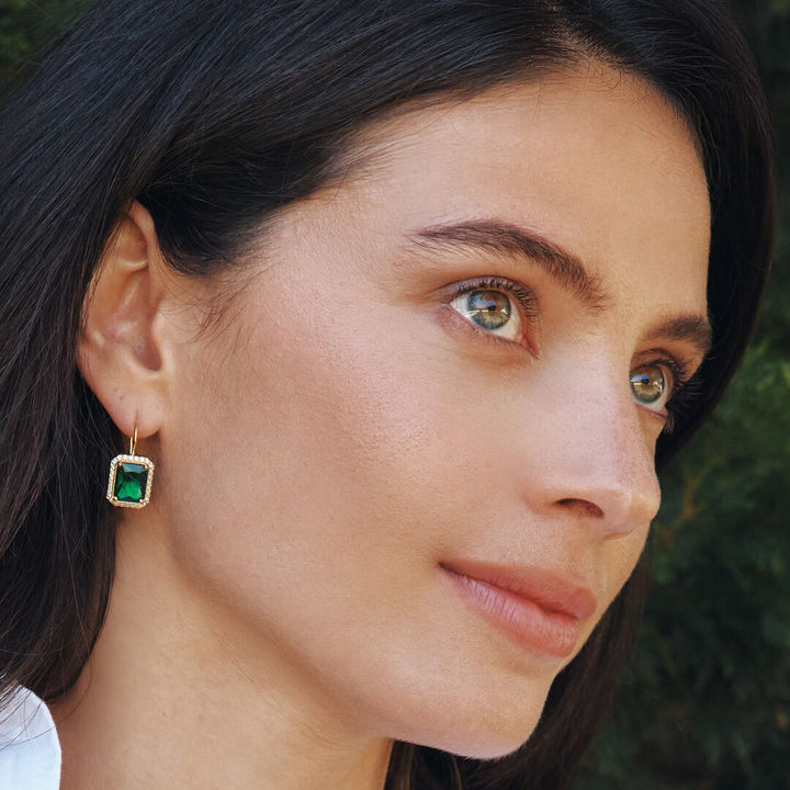 Close-up of a woman wearing emerald green earrings with a blurred natural background