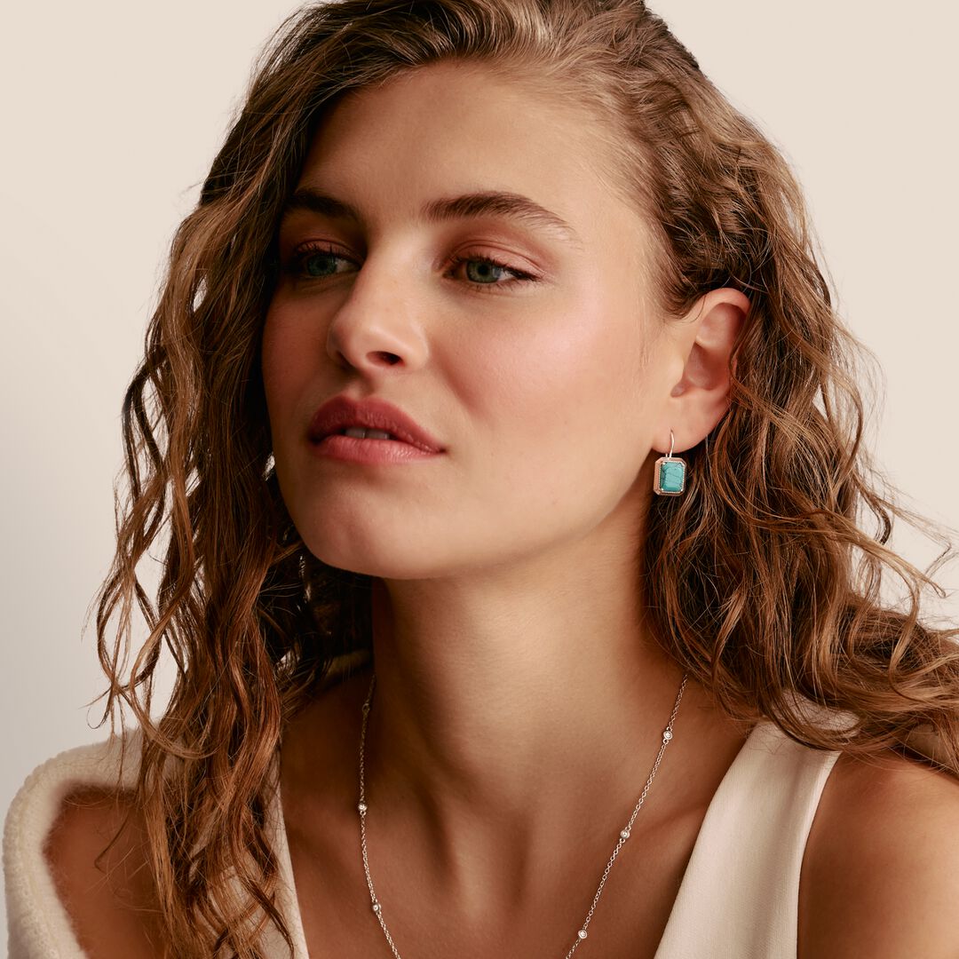 Woman with wavy hair wearing a necklace and earrings against a neutral background
