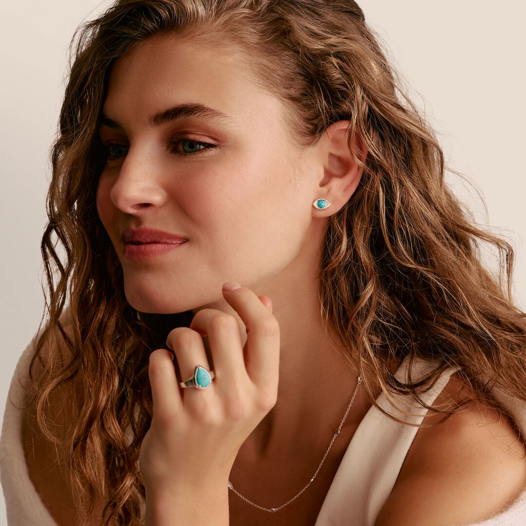 Woman wearing turquoise earrings and ring, with a neutral background