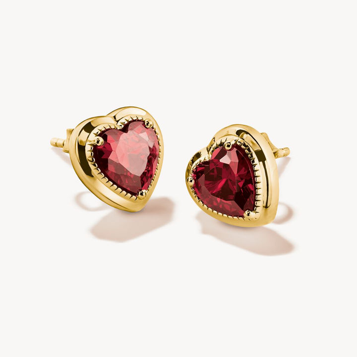 Gold heart-shaped earrings with red gemstones on a white background