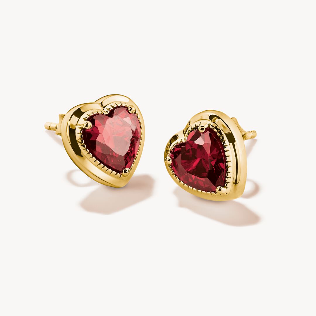 Gold heart-shaped earrings with red gemstones on a white background