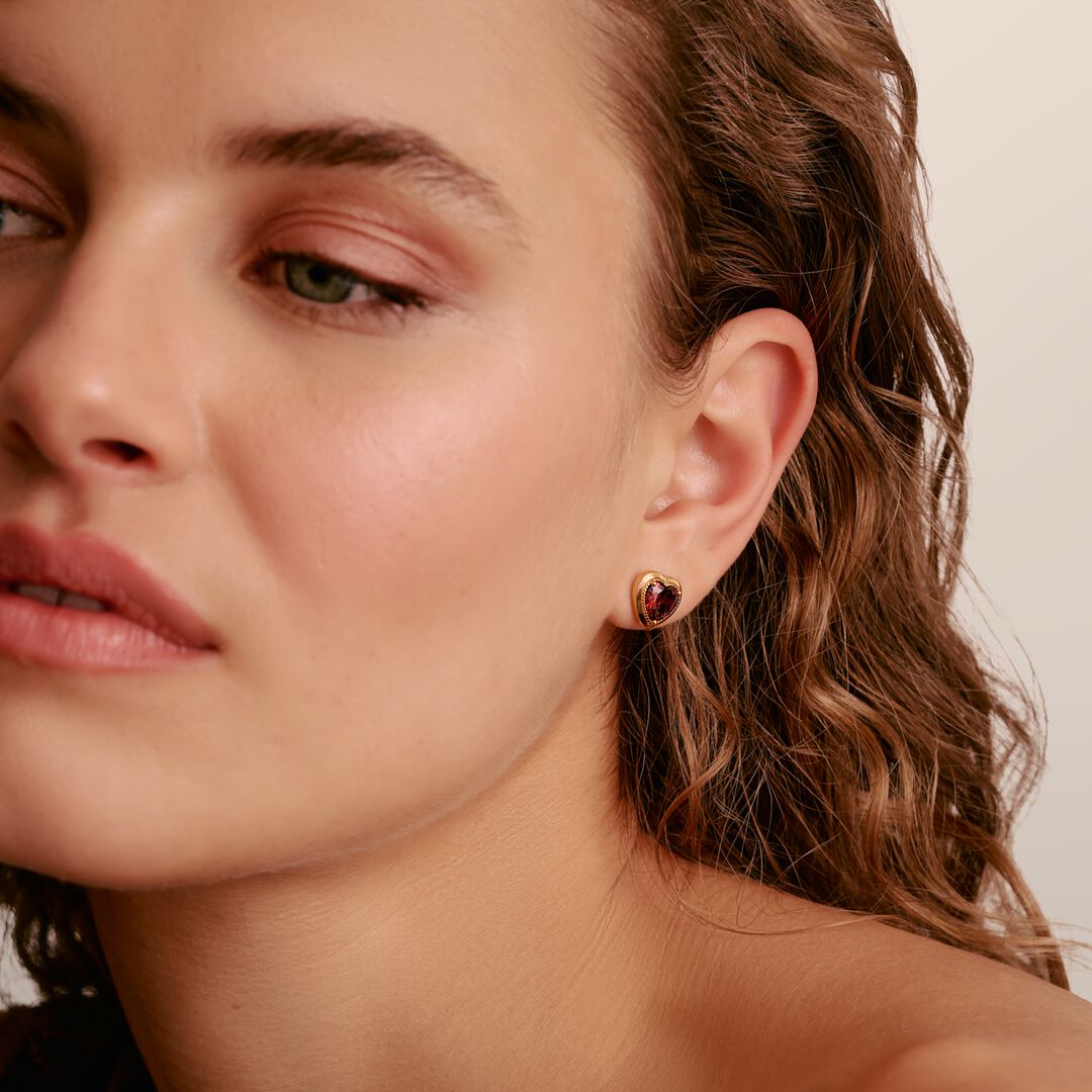 Close-up of a woman wearing a gold earring with a red gemstone on a neutral background