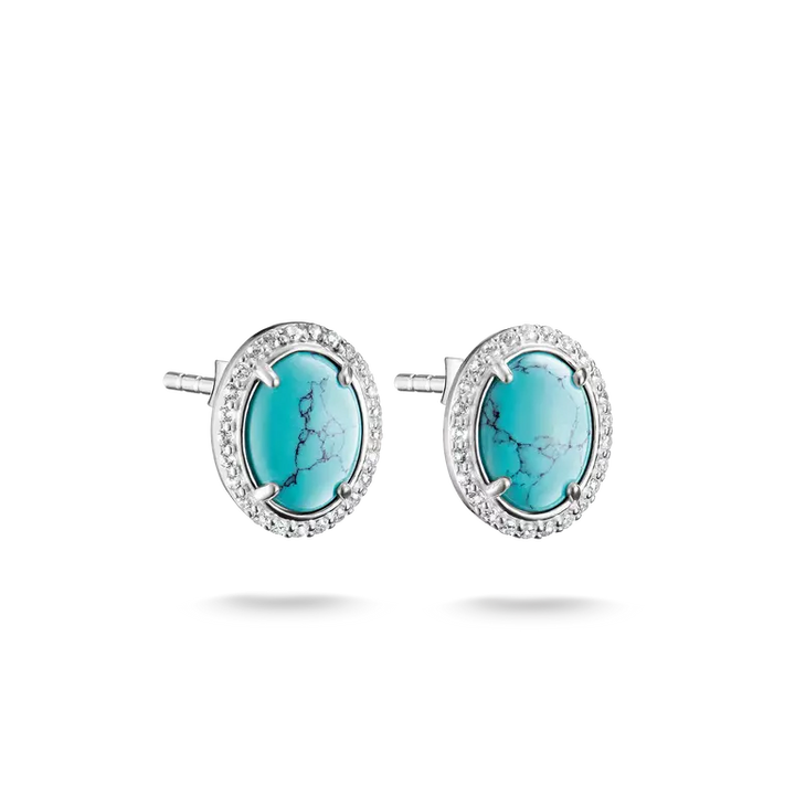 A pair of oval stud earrings featuring turquoise-colored cabochon stones surrounded by a halo of small clear stones in a silver-toned setting, shown against a plain white background.