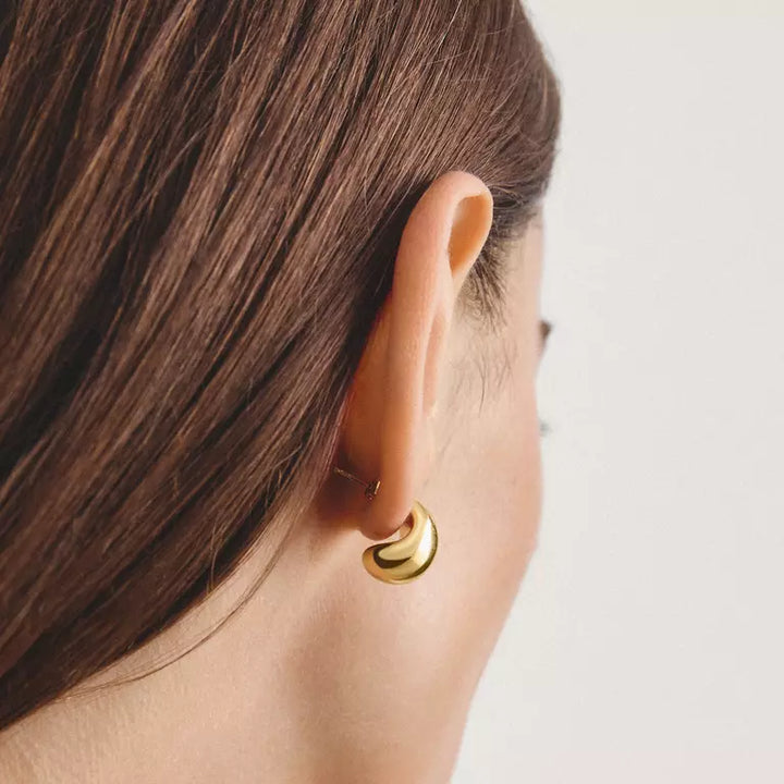 A close-up side profile of a woman with brown hair wearing a small, polished gold crescent moon hoop earring.
