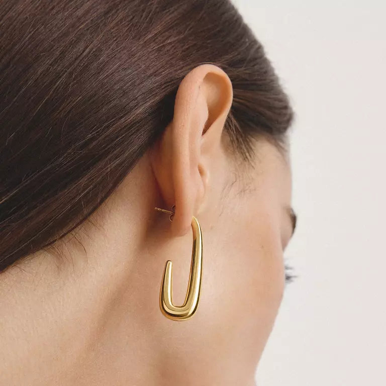 A close-up side profile of a model wearing a polished gold huggie hoop earring.