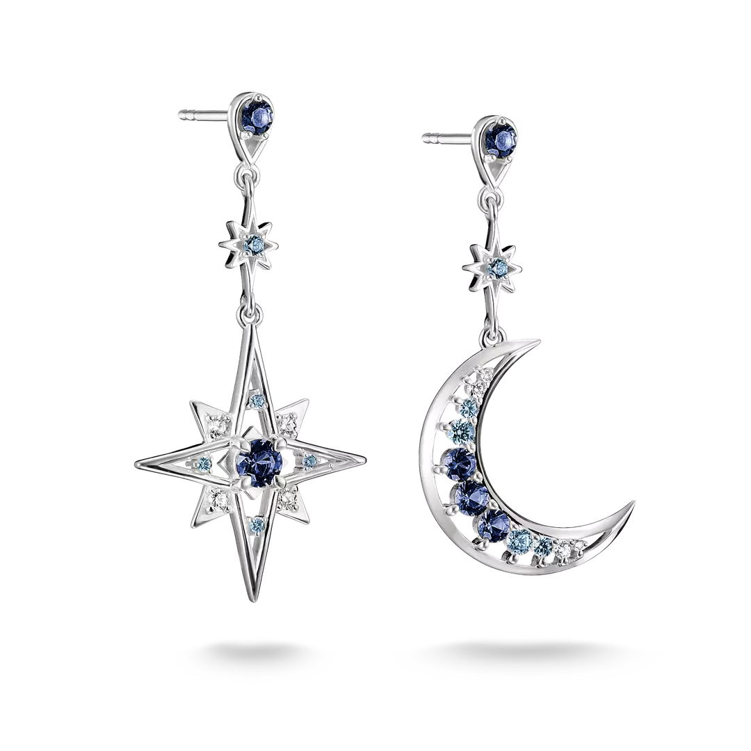 A pair of silver-toned dangle earrings featuring a large star and a crescent moon, both adorned with dark blue round gemstones and small light blue cubic zirconia accents, shown on a white background.