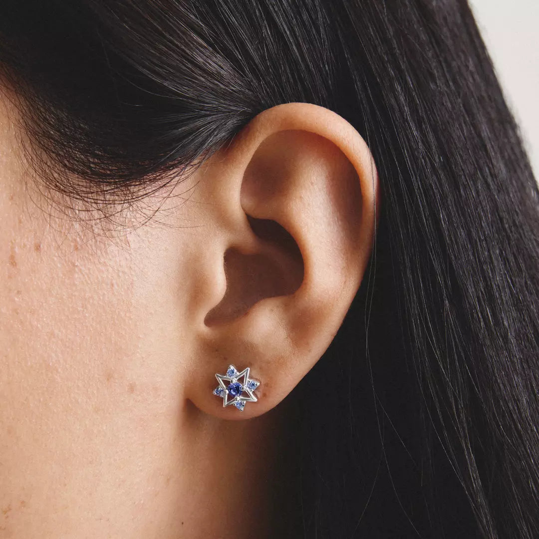 A close-up of a person's ear wearing a small star-shaped stud earring with blue stones and silver-toned metal.