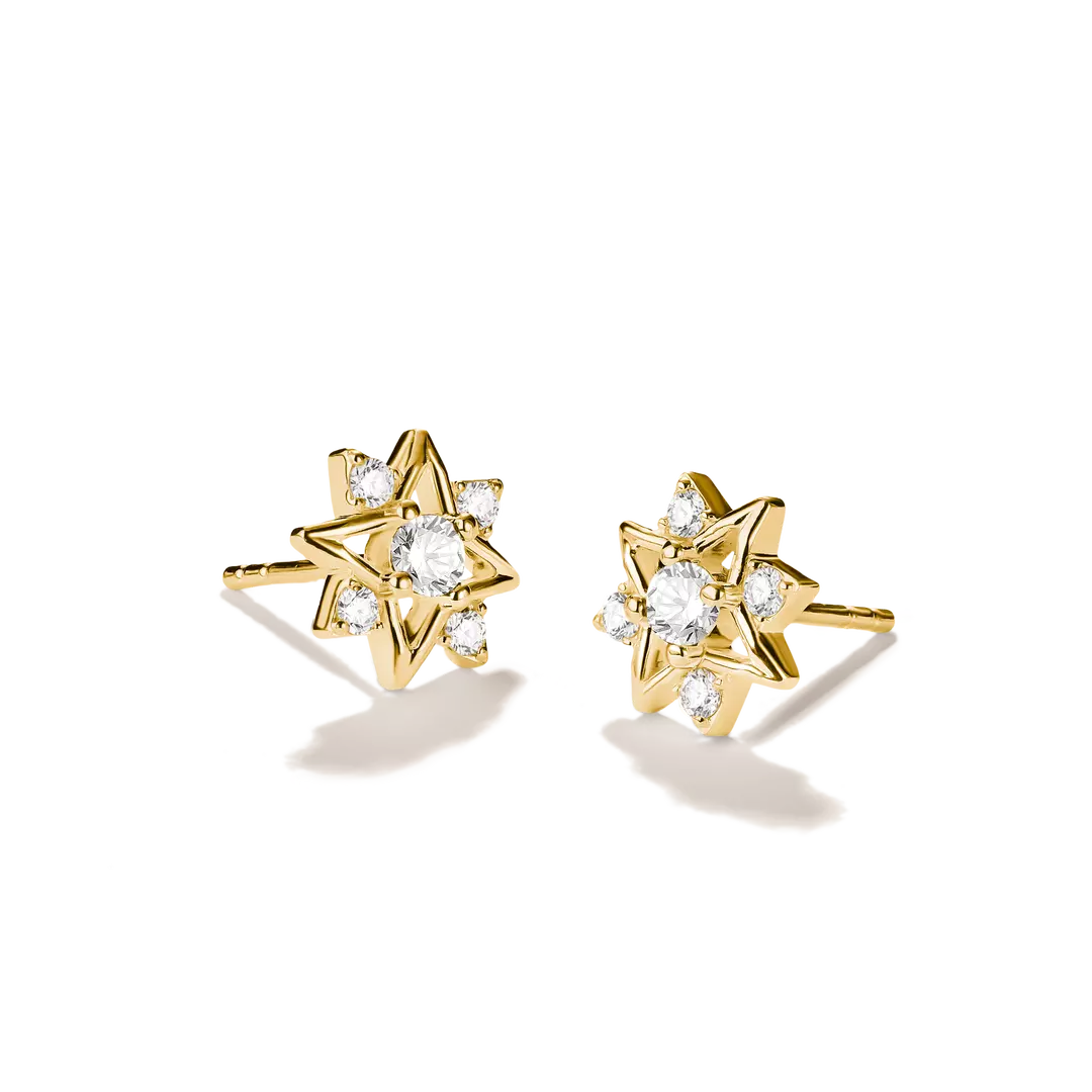 A pair of gold starburst stud earrings with clear gemstones, displayed on a clean white background with soft shadows.
