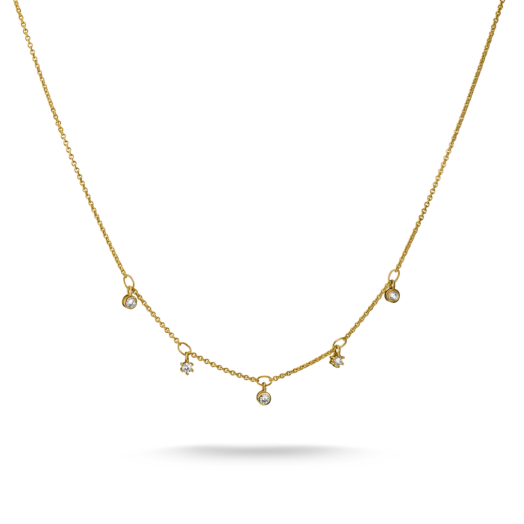 A delicate gold chain necklace featuring five small, spaced-out round clear gemstone pendants on a white background with a soft shadow underneath.