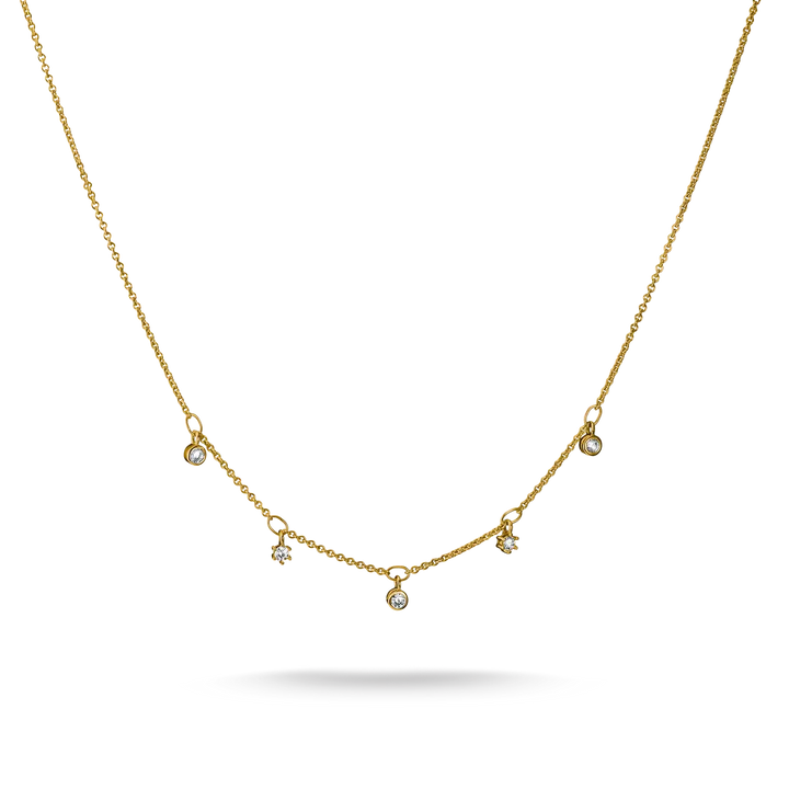 A delicate gold chain necklace featuring five small, spaced-out round clear gemstone pendants on a white background with a soft shadow underneath.