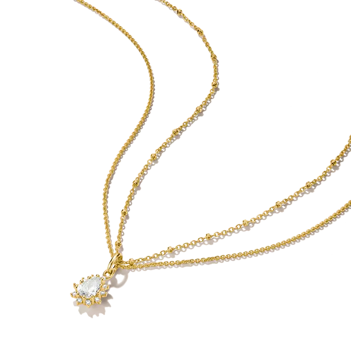 A gold double-strand necklace featuring a delicate beaded chain and a pendant with a clear teardrop-shaped gemstone surrounded by small gold stars, set against a plain white background.