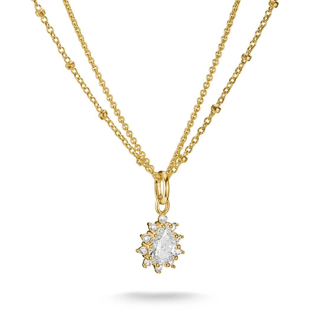 A gold double-strand necklace featuring a delicate chain and a central pendant with a pear-cut clear gemstone surrounded by small round stones in a gold setting, shown on a white background.
