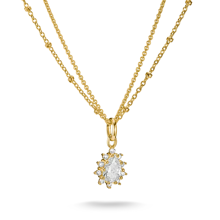 A gold double-strand necklace featuring a delicate chain and a central pendant with a pear-cut clear gemstone surrounded by small round stones in a gold setting, shown on a white background.