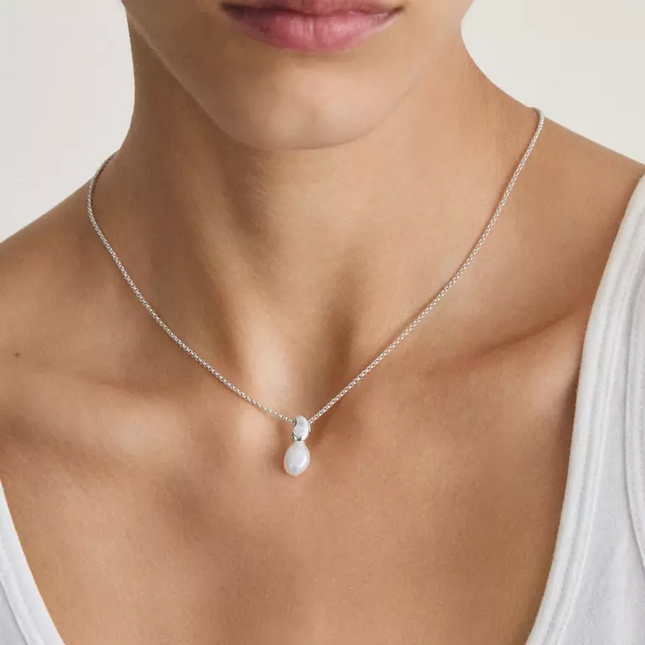 A close-up of a model wearing a delicate silver chain necklace with a small white teardrop-shaped pearl pendant.