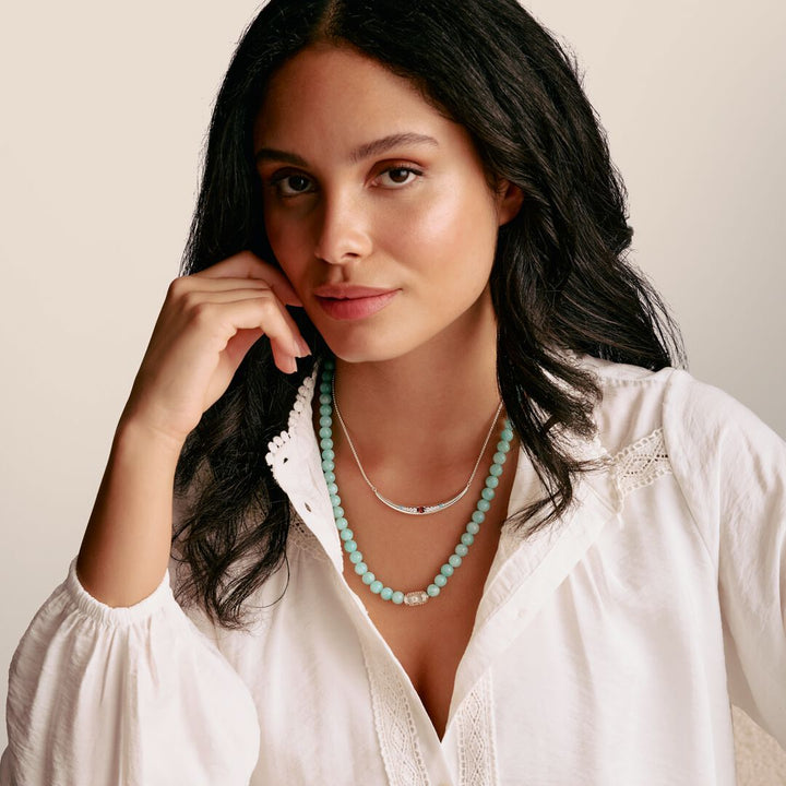 Woman wearing a white blouse and turquoise necklace against a beige background
