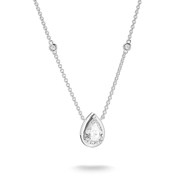 A silver-toned necklace featuring a pear-cut clear gemstone pendant in a prong setting, with a delicate chain accented by two small round bezel-set stones, shown on a white background with a soft shadow.